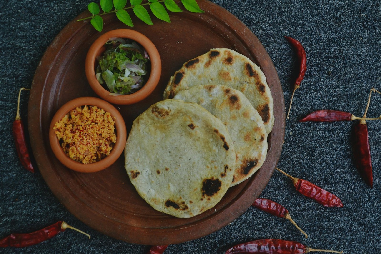 A sharing platter of freshly griddled flatbread, sambols and dried chillies laid out on a dark table.
